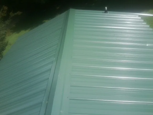 New green metal panels meeting at the ridge of a roof — Flat Roof Repair work by our crew in Spring House