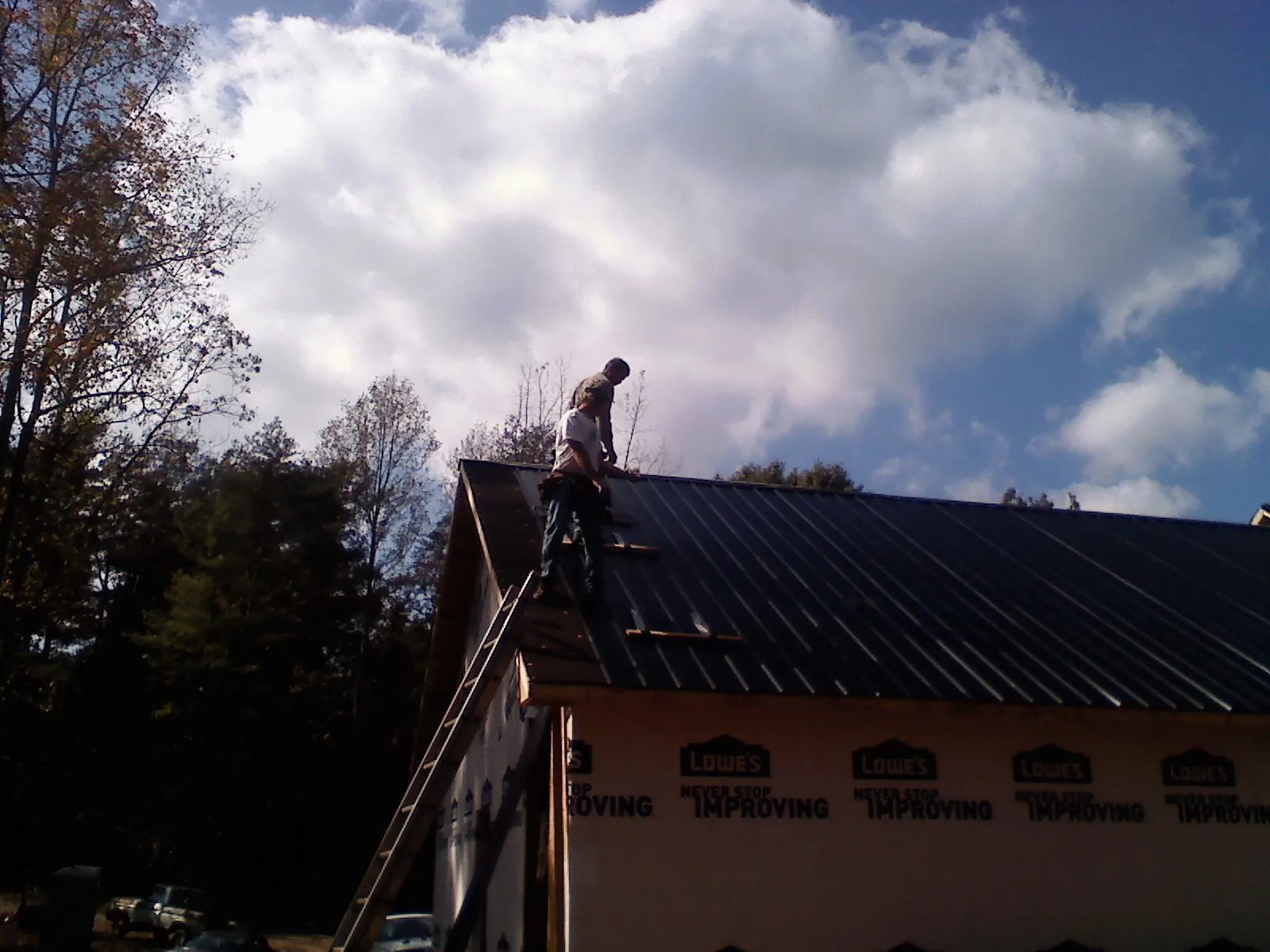 Roofer fastening dark metal panels high against a cloudy sky, from a Roof Inspection job in Spring House