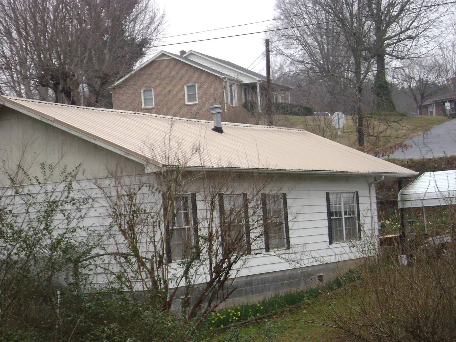 Tan metal roof on a white sided house set into a hillside — Commercial Roofing by Roofing Brothers in Spring House